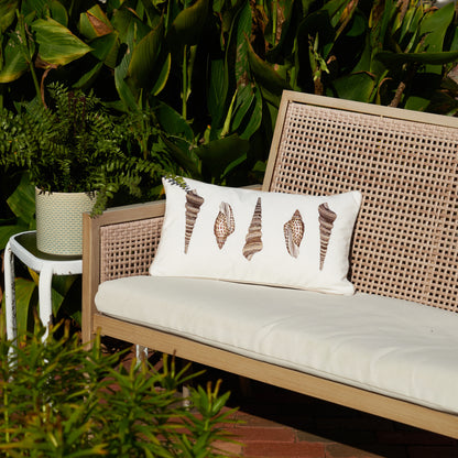 Neutral Shells Embroidered Indoor Outdoor Lumbar Pillow on Bench Surrounded by Greenery